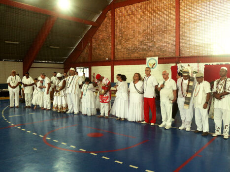 Lideranças da Associação Sábios da Paz reunidas em fila - uma pessoa ao lado da outra. Estão de branco, na Quadra de Esportes.